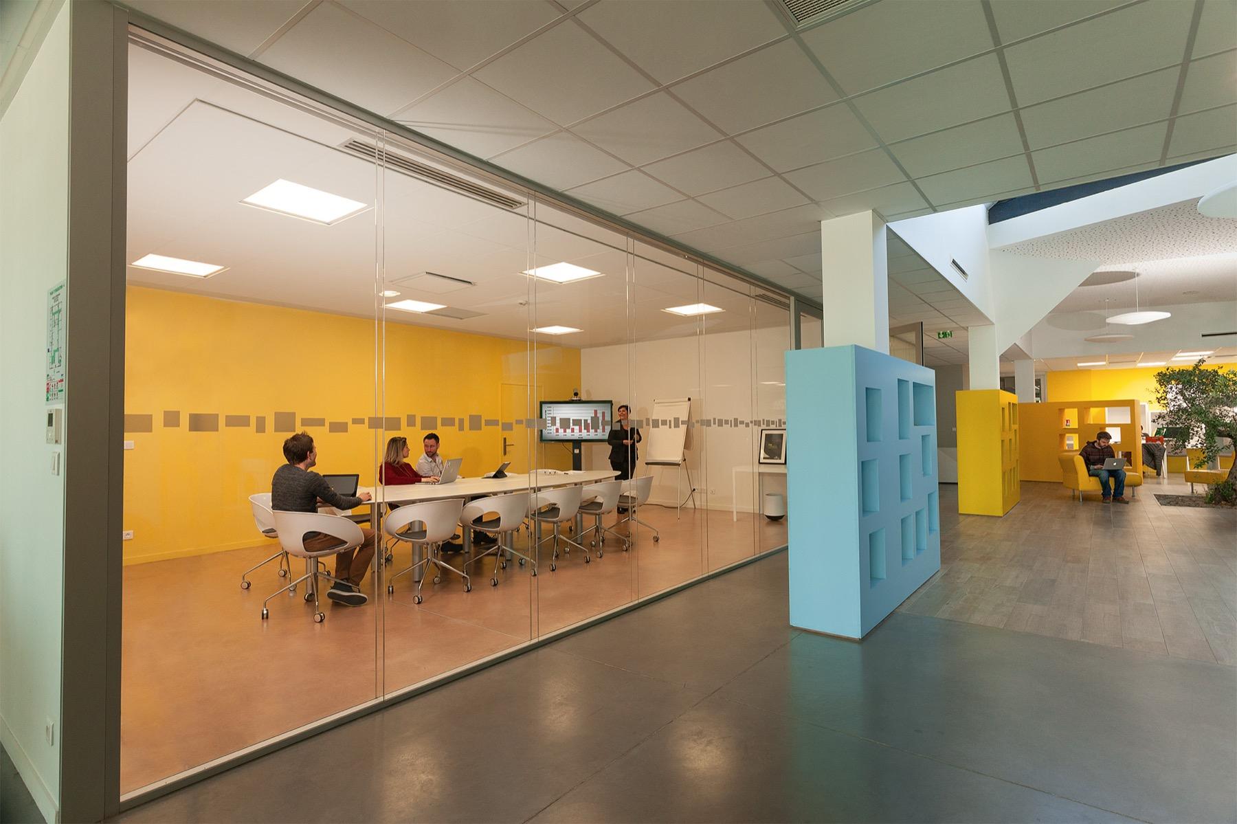 Open Plan — Salle de réunion vitrée aux murs jaunes dans un espace de coworking moderne