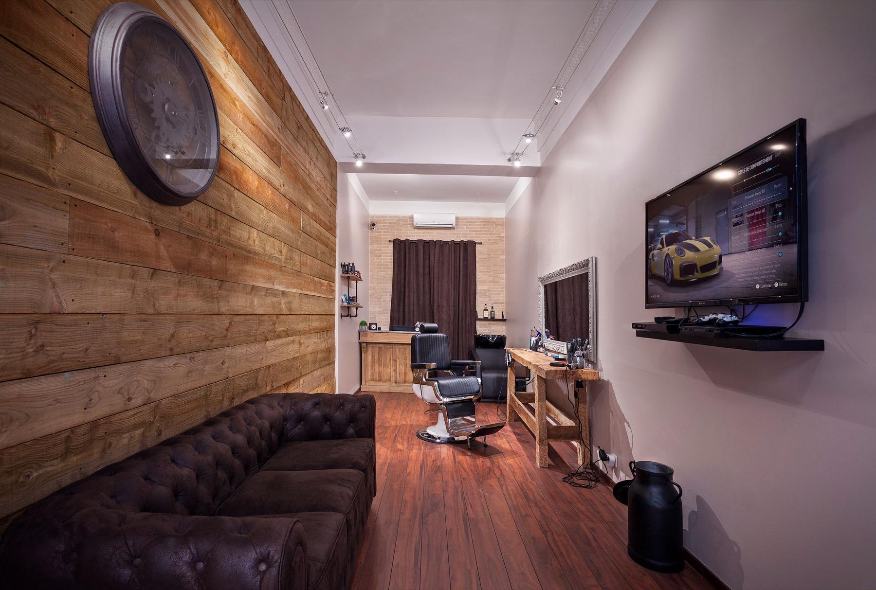 Le Salon — Intérieur du salon de barbier Le Garçon : mur en lames de bois, canapé Chesterfield et fauteuil de barbier
