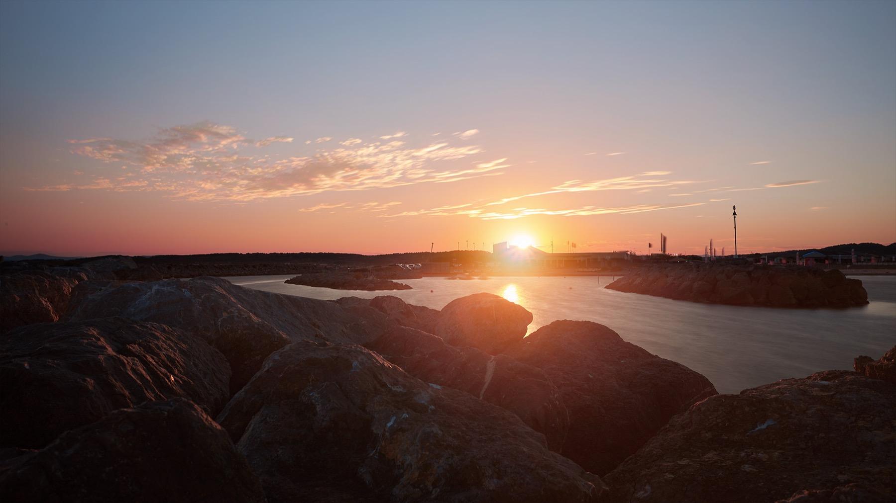 Last Light — Soleil couchant sur une étendue d’eau calme, rochers au premier plan