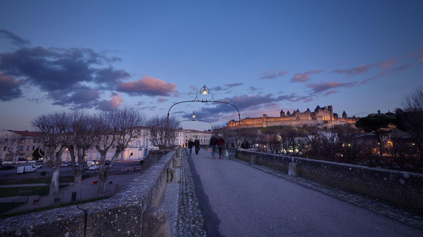 Blue Hour — Pont pavé à l’heure bleue menant vers une cité médiévale fortifiée illuminée
