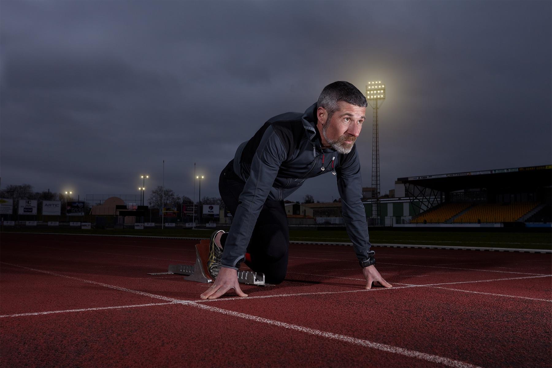Night Lane — Coureur accroupi dans les starting-blocks sur une piste d’athlétisme éclairée de nuit